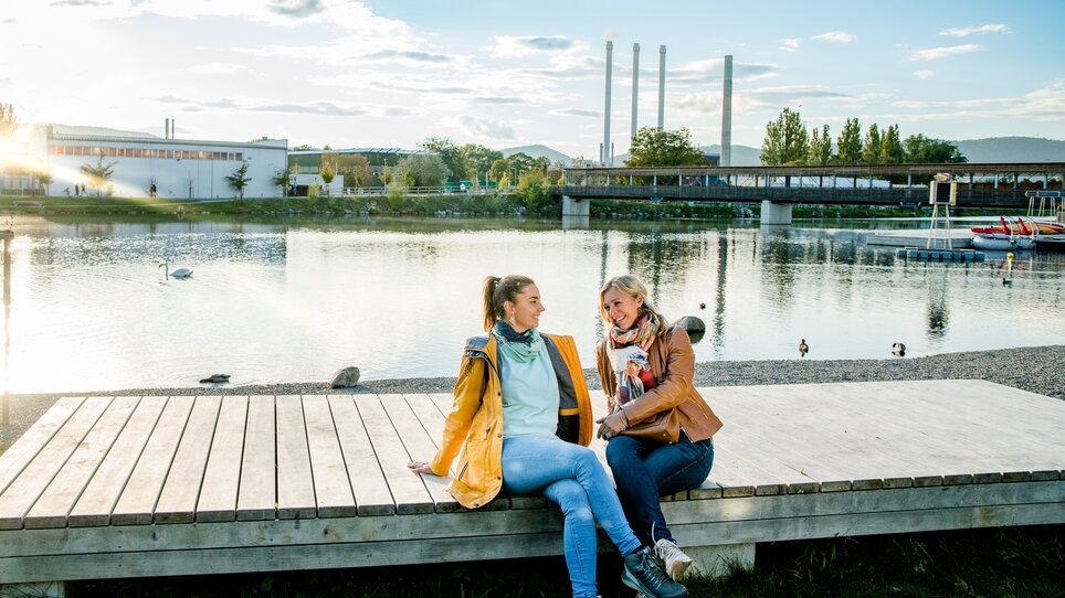 Zwei Frauen entspannen am Ufer der Mur in Graz, umgeben von Natur. | © Graz Tourismus
