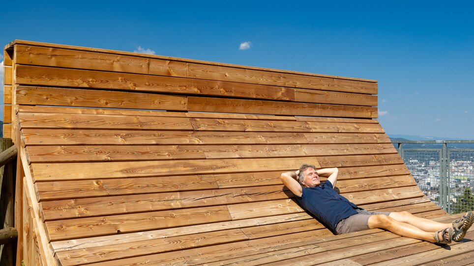 A person relaxes on a wooden deck overlooking Graz. | © Graz Tourismus