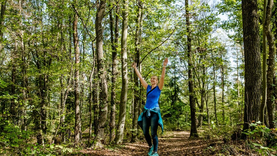 Eine Frau genießt einen sonnigen Tag im Wald und hebt die Hände in die Luft. | © Graz Tourismus