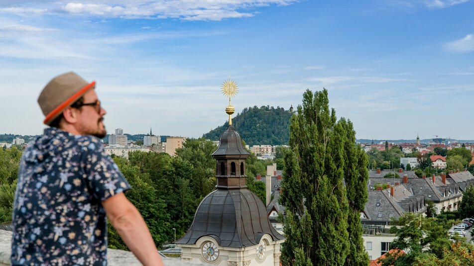 Mann blickt über Graz mit dem Grazer Schlossberg im Hintergrund. | © Graz Tourismus