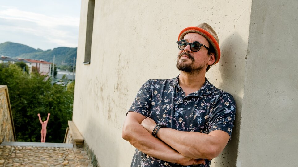 Ein Mann lehnt an einer Wand, eine pinke Figur ist im Hintergrund. | © Graz Tourismus