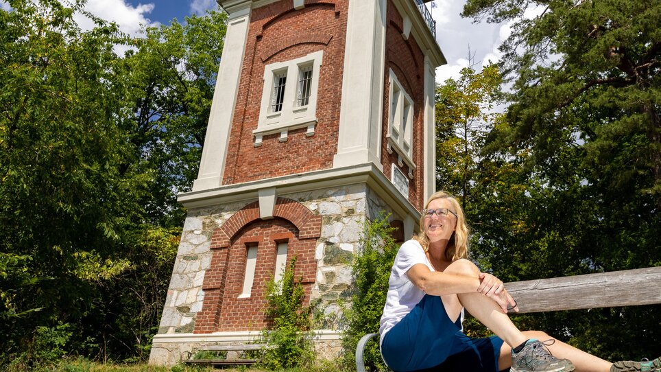 Woman sitting on a bench in front of a tower surrounded by greenery, perfect for relaxation in Graz.