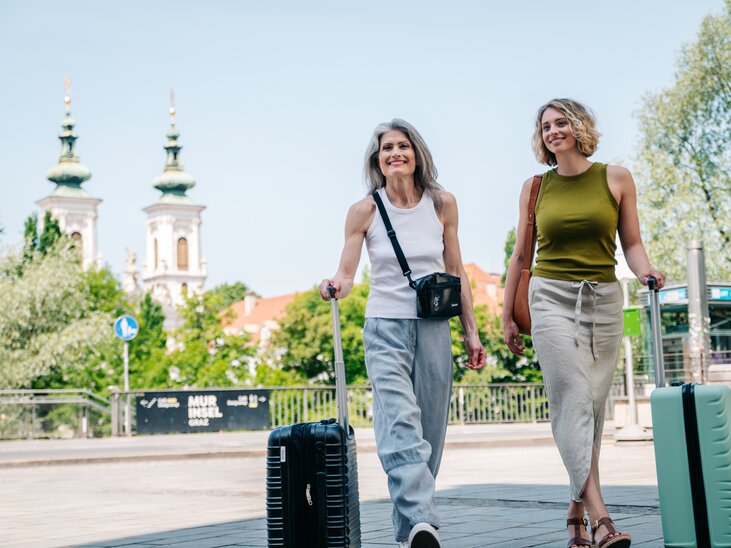 Zwei Frauen mit Koffern spazieren durch Graz bei schönem Wetter. | © Graz Tourismus - Mias Photoart