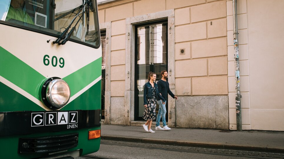 Ein Paar geht entspannt an einer Straßenbahn in Graz vorbei. | © Graz Tourismus
