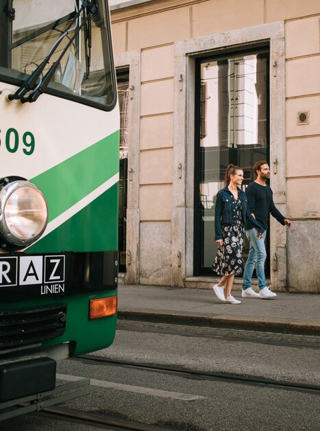 Ein Paar geht entspannt an einer Straßenbahn in Graz vorbei. | © Graz Tourismus