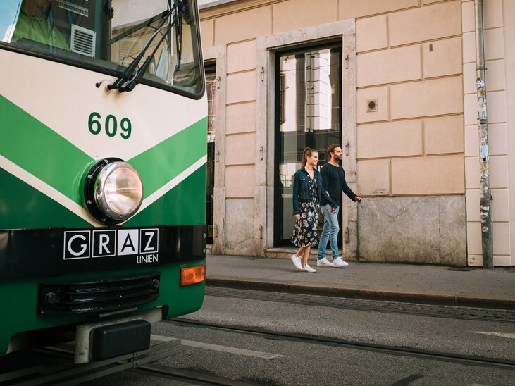 Una coppia passeggia lentamente accanto a un tram a Graz. | © Graz Tourismus