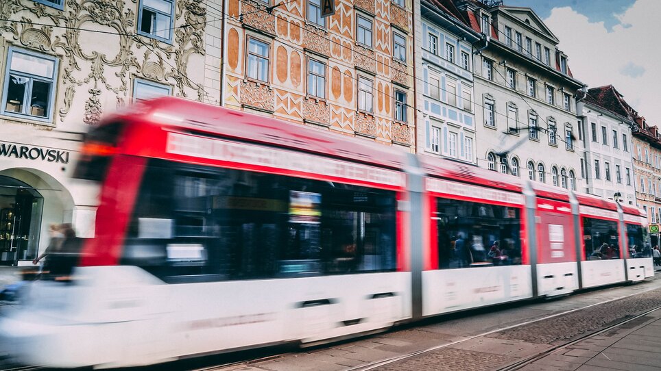 Eine Straßenbahn in Graz fährt an einer bunten Fassade am Grazer Hauptplatz vorbei. Der Swarovski Shop ist im Hintergrund zu sehen. | © Janet Newenham-Journalist on the Run