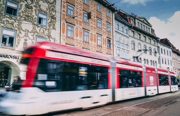 Eine Straßenbahn in Graz fährt an einer bunten Fassade am Grazer Hauptplatz vorbei. Der Swarovski Shop ist im Hintergrund zu sehen. | © Janet Newenham-Journalist on the Run