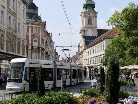 A tram in Graz with the City Parish Church in the background and blooming flowers in the foreground. | © Jasminka Putopis