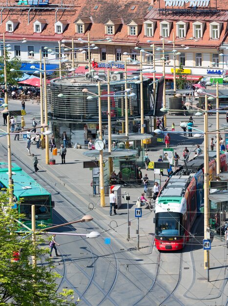 Bright square in Graz featuring a tram surrounded by cafés and shops. | © Graz Tourismus - Harry Schiffer