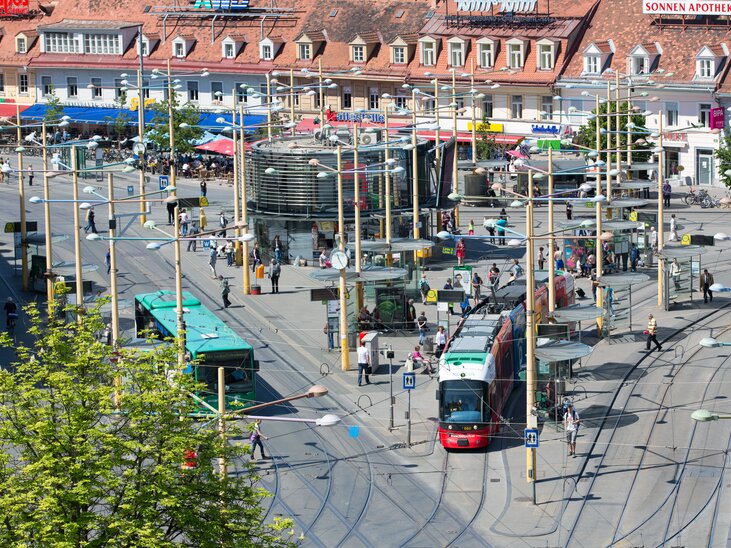 Bright square in Graz featuring a tram surrounded by cafés and shops. | © Graz Tourismus - Harry Schiffer