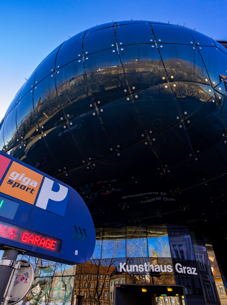 Il moderno Kunsthaus Graz riflette l'ambiente circostante con un cartello per il parcheggio. | © Graz Tourismus - Harry Schiffer