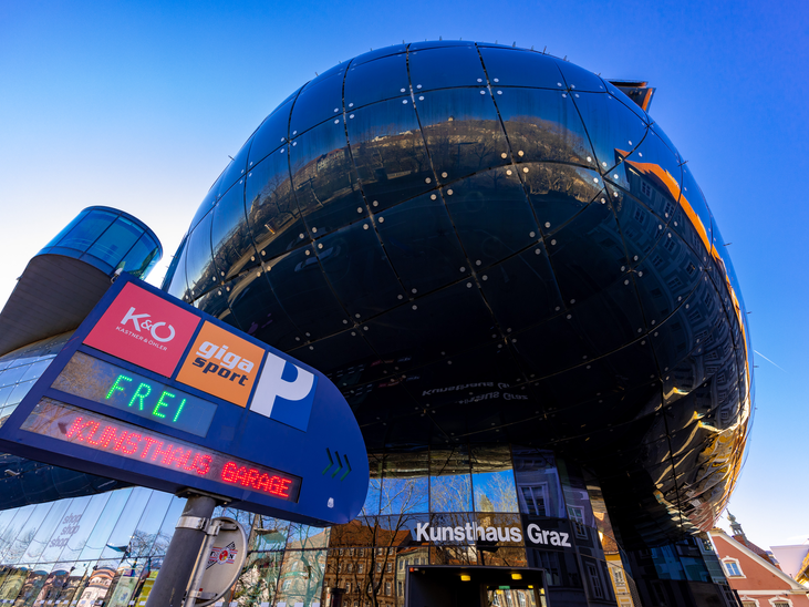 Das moderne Kunsthaus Graz spiegelt die Umgebung wider mit einem Parkplatz-Schild. | © Graz Tourismus - Harry Schiffer