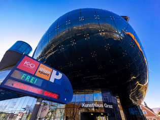 Das moderne Kunsthaus Graz spiegelt die Umgebung wider mit einem Parkplatz-Schild. | © Graz Tourismus - Harry Schiffer