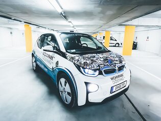 Una BMW i3 elettrica in un parcheggio con pubblicità. | © 111 gröbl wohnpark gösting entwicklungs gmbh