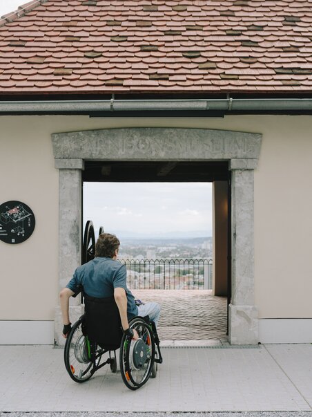Uomo in sedia a rotelle al Museo Schlossberg di Graz con vista sui tetti di Graz | © Sebastian Reiser