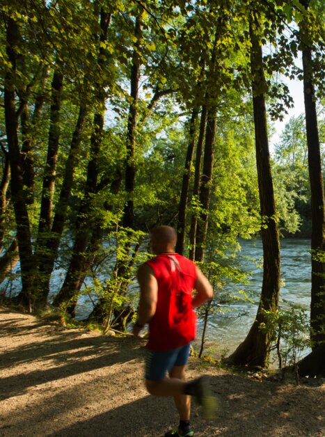 Ein Läufer joggt entlang des Flusses Mur, umgeben von Bäumen. | © Graz Tourismus - Harry Schiffer