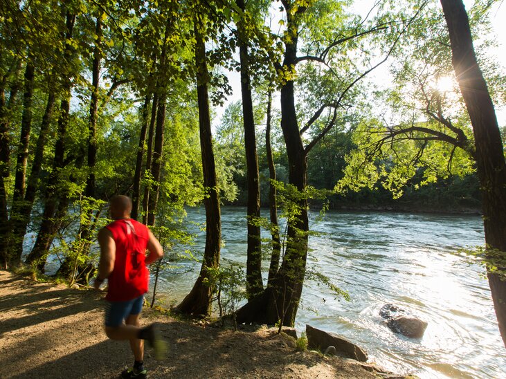 Un corridore fa jogging lungo il fiume Mur, circondato da alberi. | © Graz Tourismus - Harry Schiffer