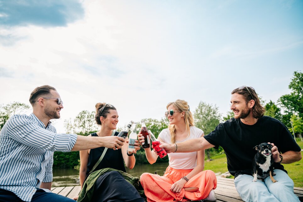 Quattro amici brindano con delle bevande in riva al fiume. | © Graz Tourismus - Mias Photoart