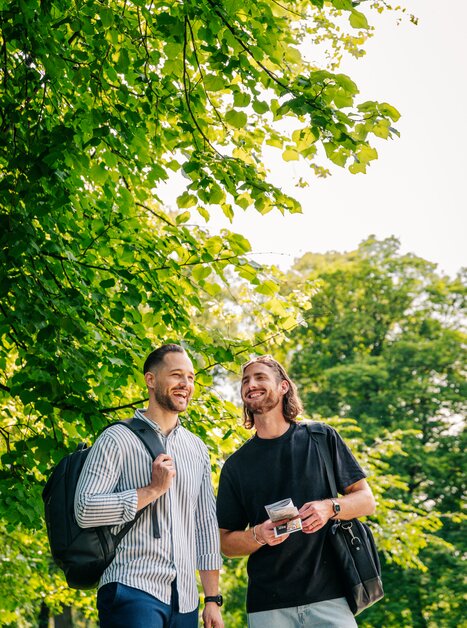 Zwei Männer stehen lächelnd im Grünen und genießen die Zeit. | © Graz Tourismus - Mias Photoart
