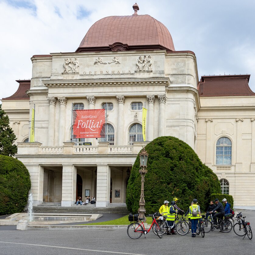 Geführte Radtour in Graz | © Graz Tourismus - Harry Schiffer Das Opernhaus in Graz mit Radfahrern davor und einem großen Plakat. | © Graz Tourismus - Harry Schiffer