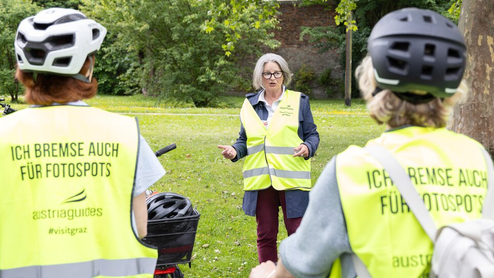 Drei Personen in Warnwesten diskutieren während einer Fahrradtour in der Natur. | © Graz Tourismus - Harry Schiffer