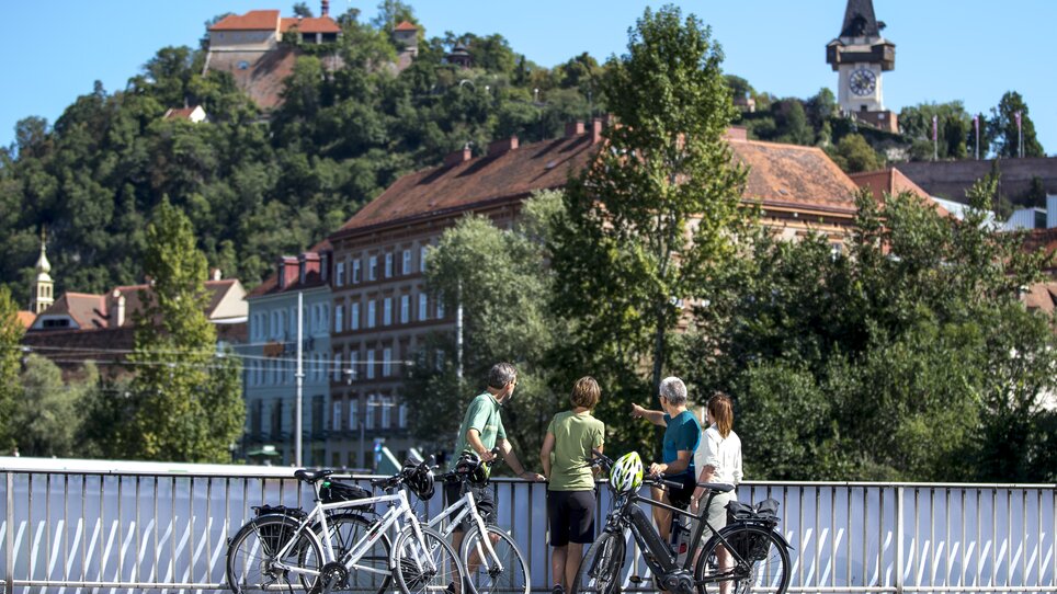 Radfahrer betrachten den Uhrturm über Graz und die Mur. | © Graz Tourismus - Tom Lamm