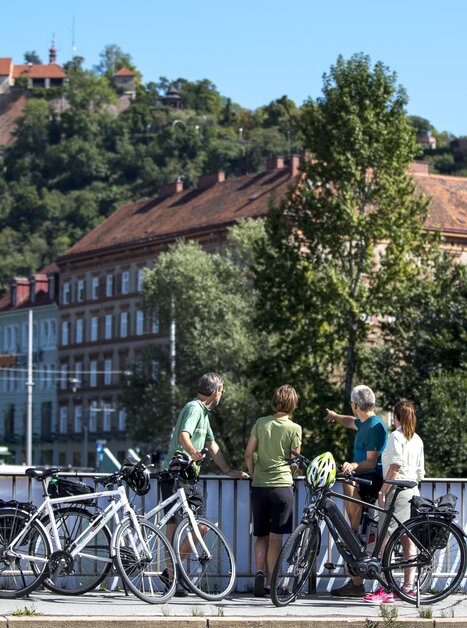Radfahrer betrachten den Uhrturm über Graz und die Mur. | © Graz Tourismus - Tom Lamm
