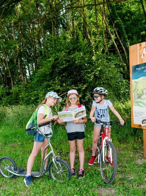 Drei Kinder mit einem Roller und Fahrrad betrachten eine Karte in der Natur. | © Erlebnisregion Graz