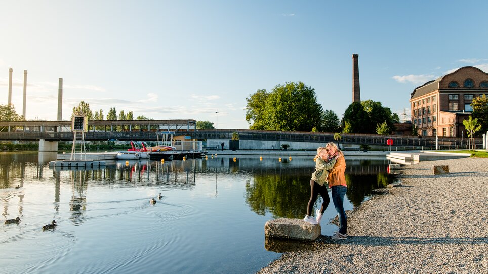 Mutter und Tochter umarmen sich am Ufer der Mur beim Stadtstrand in Graz bei Sonnenuntergang. | © Graz Tourismus - Mias Photoart