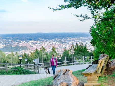 A woman walks with her dog on a path overlooking Graz. | © Graz Tourismus - Mias Photoart