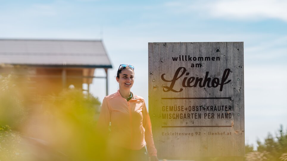 Frau steht vor dem Willkommensschild am Lienhof. | © Graz Tourismus - Mias Photoart