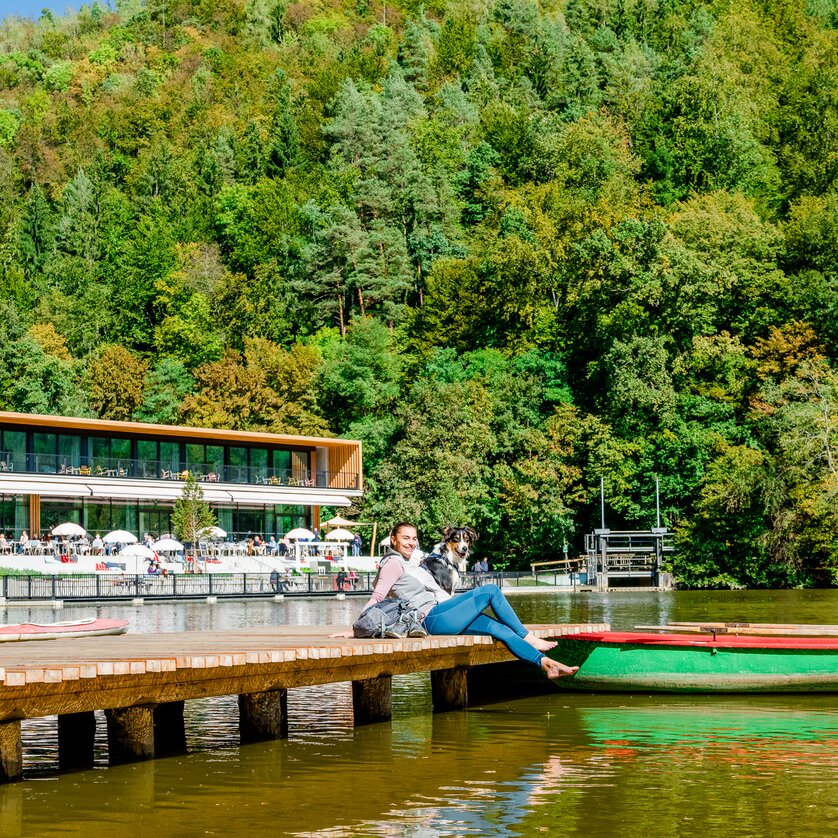 Eine Frau sitzt am Steg am Thalersee mit ihrem Hund. | © Graz Tourismus - Mias Photoart