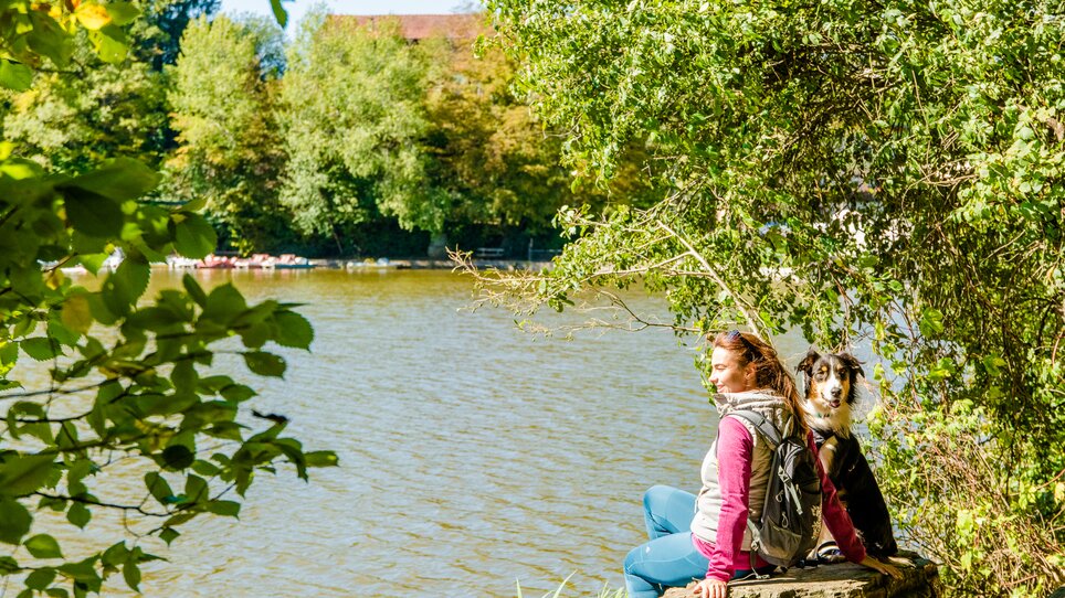 Ein Mensch sitzt am Thalersee mit einem Hund in der Natur. | © Graz Tourismus - Mias Photoart