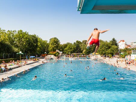 Un ragazzo salta nella piscina dell'Augartenbad Graz in una giornata di sole. | © Holding Graz - Joel Kernasenko
