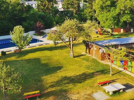Green meadow with picnic tables and swimming pool in the background. | © Ragnitzbad