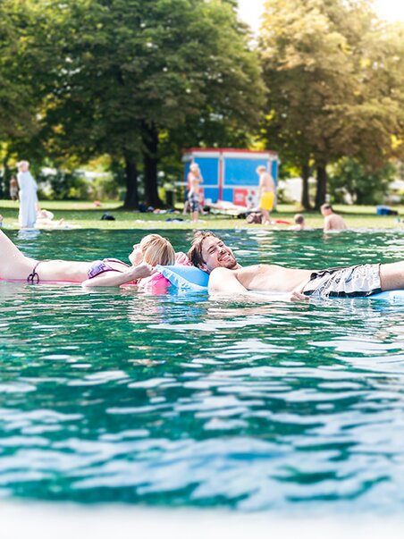 Coppia che naviga su materassini nel Bad Straßgang, Graz, in una giornata di sole. | © Holding Graz - Joel Kernasenko