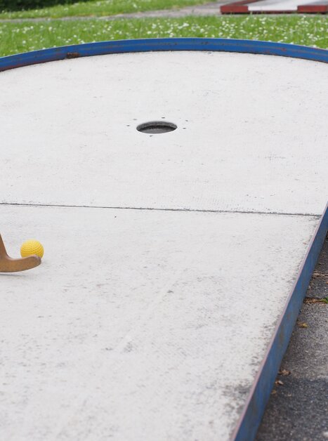 Primo piano di un campo da mini golf con palla gialla e mazza di legno. | © Pixabay