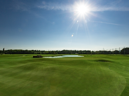 Expansive golf course with green grass and a water feature under bright sun. | © GC Grazer MurAuen