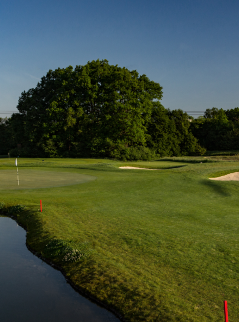 Campo da golf verde con stagno e bunker sabbiosi sotto un cielo sereno. | © GC Grazer MurAuen