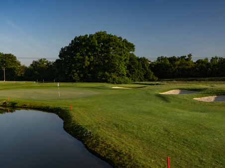 Green golf course with pond and sand bunkers under clear sky. | © GC Grazer MurAuen