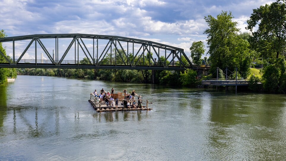 Raft on the Mur in Graz with passengers and bridge in the background. | © Harry Schiffer