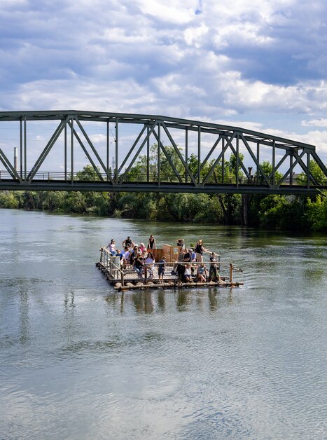 Raft on the Mur in Graz with passengers and bridge in the background. | © Harry Schiffer