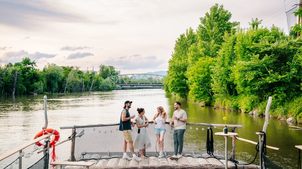 Gruppe von Freunden genießt Zeit am Fluss in Graz, umgeben von Bäumen. | © Graz Tourismus - Mias Photoart