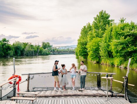 Group of friends enjoying time by the river in Graz, surrounded by trees. | © Graz Tourismus - Mias Photoart