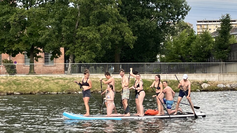 Gruppo che pratica stand up paddle sul fiume Mur a Graz. Divertimento sull’acqua. | © Die Flößerei