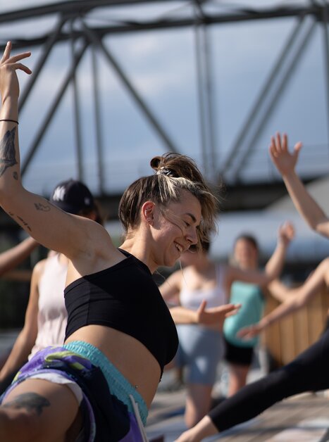 A group of people is taking part in a yoga class on a raft on the Mur River in Graz, offered by “Der Flößerei”. | © Robert Supnig