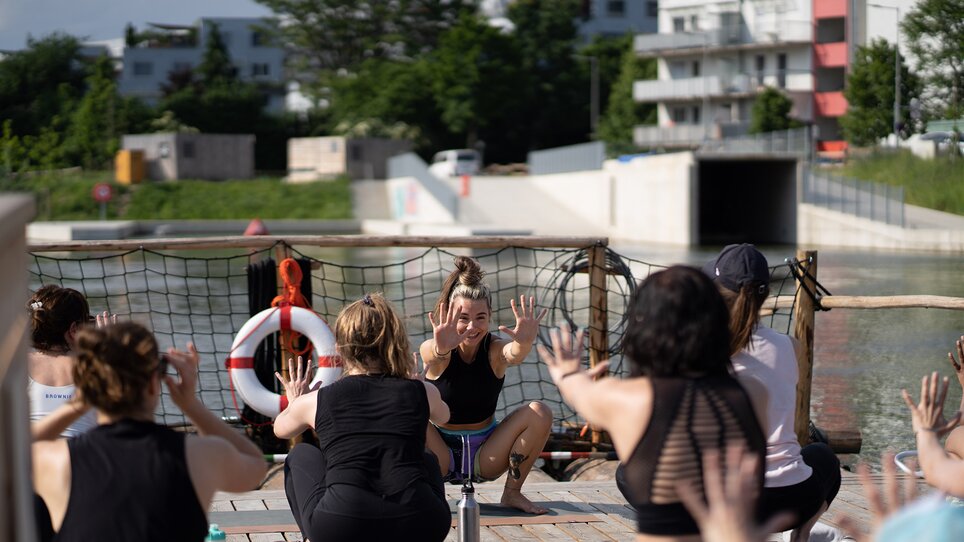 A group of people is taking part in a yoga class on a raft on the Mur River in Graz, offered by “Der Flößerei”. | © Robert Supnig