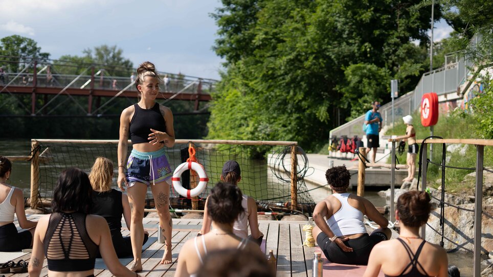 A group of people is taking part in a yoga class on a raft on the Mur River in Graz, offered by “Der Flößerei”. | © Robert Supnig