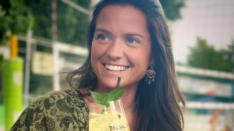 Eine Frau mit einem Getränk in der Hand, lächelnd am Mur Beach in Graz. | © Mur Beach - Ingo Gruber